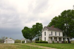 Old white 2 story frsme fsrmhouse with porch and shed